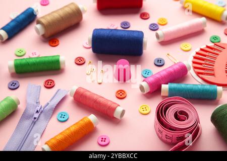 Sewing supplies on pink background: sewing thread, scissors, a large spool of thread, pieces of cloth, needles,centimeter, buttons. Top view Stock Photo