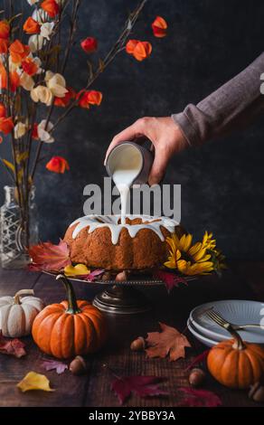 Hand pouring icing glaze on pumpkin spice bundt cake for fall. Stock Photo