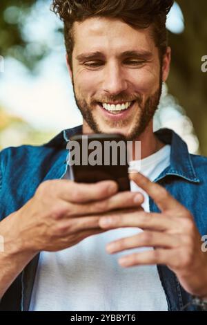Happy man, typing and browsing with phone in nature for social media, chatting or texting app. Young, male person or user with smile on mobile Stock Photo