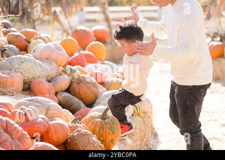 Father helping son up hay stacks and pumpkins Stock Photo