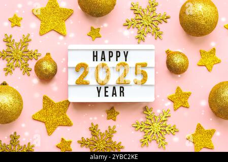 Happy new year 2025.Top view of lightbox with the word Happy new year 2025,golden christmas balls and golden stars over pink background. New Years Eve Stock Photo