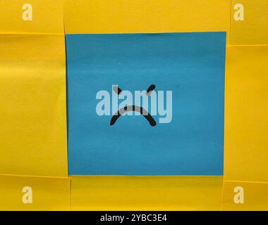 Emotional Contrast. Blue Face Sticky Note with Angry Expression Against a Yellow Background. Stock Photo