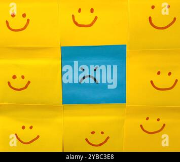 Emotional Contrast. Blue Face Sticky Note with Angry Expression surrounded by yellow smiley faces. Stock Photo