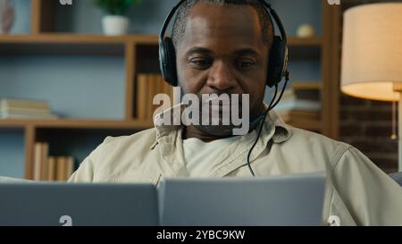 African American man male businessman sales manager freelancer homeowner working on laptop at home using headset checking documents paying bills Stock Photo