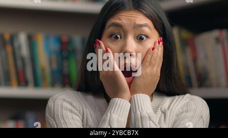 Amazed excited shocked stressed asian woman girl student teacher worried about bad news frightened expression open mouth feeling stress in library Stock Photo