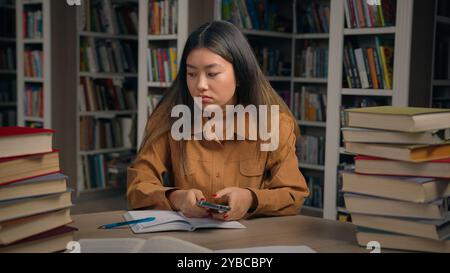 Sad frustrated stressed asian woman girl in university library checking email reading bad news on mobile phone disappointed chinese female student Stock Photo