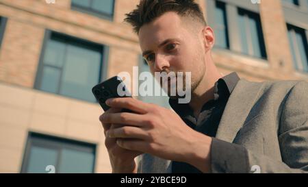 Surprised amazed Caucasian man receiving email message on phone in city outdoors shocked male guy businessman reading news on social network in Stock Photo