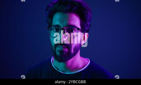 Close up portrait neon ultraviolet background Indian man guy developer coder smart hacker clever coding computer engineer showing gesture think about Stock Photo
