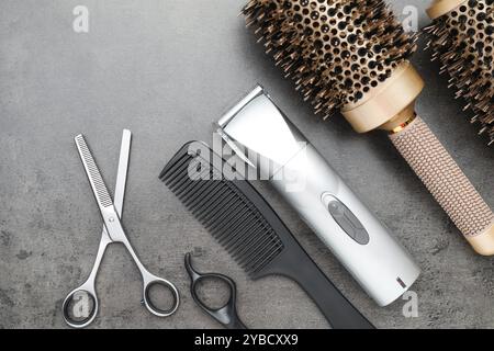 Professional hair clipper, different combs and scissors on grey surface, flat lay Stock Photo