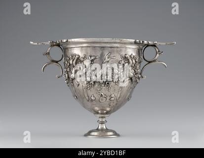 Skyphos, 50-25 B.C.  Additional Info: Four flying Cupids support a large continuous garland that wraps around this Roman silver skyphos, one of a pair of matching cups. The two cups are not identical, however, for the cupids on each differ slightly in their posture and placement. Wound with ribbons, the garland is rich with fruits, including pomegranates, grapes, olives, and pinecones. Birds perch on and hover over the garland, while various items hang from it: tympana (drums), cistae (wicker baskets), auloi (double pipes), and cymbals, all instruments associated with the cult of the wine-god Stock Photo