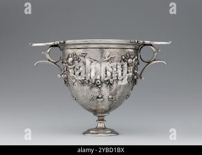 Skyphos, 50-25 B.C.  Additional Info: Four flying Cupids support a large continuous garland that wraps around this Roman silver skyphos, one of a pair of matching cups. The two cups are not identical, however, for the Cupids on each differ slightly in their posture and placement. The garland is wound with ribbons and rich with fruits, including pomegranates, grapes, olives, and pinecones. Birds perch on and hover over the garland, while various items hang from it: tympana (drums), cistae (wicker baskets), auloi (double pipes), and cymbals, all instruments associated with the cult of the wine-g Stock Photo