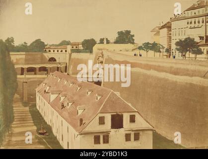 View from the Waterworks to the Powder Magazine and the bridges of the Old and New Kärntnertor Gates, 1858. A long building with shuttered windows at the base of a high wall. Three men are standing at the edge of the wall looking out. There are two arched bridges beyond the long building. Stock Photo