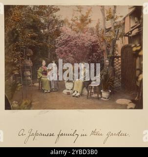 A Japanese family in their garden, about 1873-1883. Three adults and a girl seated on rocks and a chair surrounded by trees, flowering bushes, and potted plants. Stock Photo