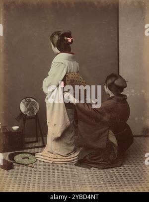 Dressing Obi, 1870s-1890s. A woman kneeling behind another woman, arranging her obi (sash). Stock Photo