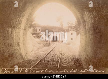 Sbocco della Galleria Valenza ed imbocco della galleria Vallerosa, October 1883. View from inside a tunnel looking down a set of train tracks towards a second tunnel in a small hillside. Three figures are scattered around the tracks on both sides, and two smaller buildings flank the tunnel opening. Stock Photo