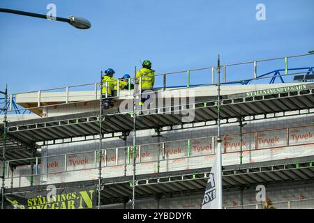 Three construction workers are engaged in installing panels on a high-rise building while working on scaffolding, ensuring safety and precision Stock Photo