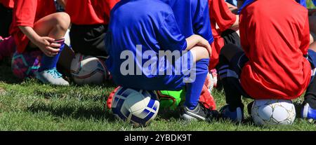 Kids preparing for their soccer training listening to the coach while sitting on their soccer balls Stock Photo