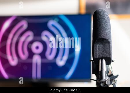 A close-up of a microphone in front of a computer setup with dual monitors displaying a podcast or broadcasting theme. Stock Photo