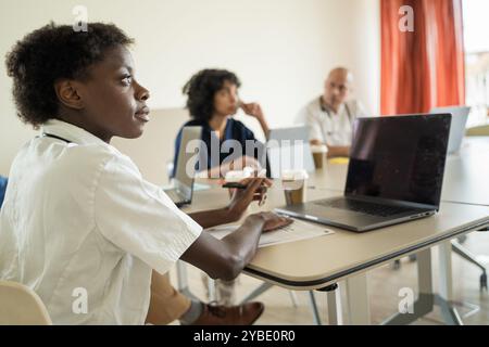 Diverse group of healthcare professionals in a meeting. African American doctor in foreground, with colleagues and laptops. Modern medical conference Stock Photo