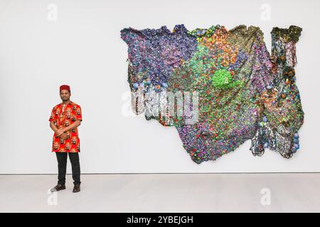 London, UK. 18th Oct, 2024. The artist with 'Fertile Soil', 2023. Saatchi Gallery present new works by Nigerian textile artist Samuel Nnorom in the solo exhibition ‘Multitude or Minority'. Nnorom's sculptures are visual metaphors made from offcuts of Ankara fabric, the wax-printed cloth now synonymous with African textiles. The exhibition will be open from 19 October to 24 November, 2024. Credit: Imageplotter/Alamy Live News Stock Photo