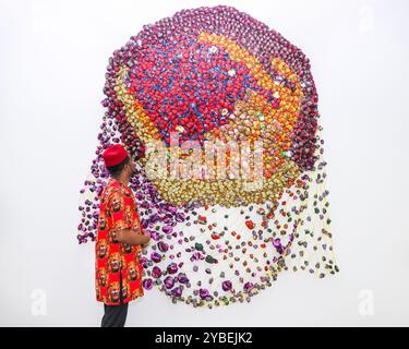 London, UK. 18th Oct, 2024. The artist with 'Sunrise After Dusk', 2023. Saatchi Gallery present new works by Nigerian textile artist Samuel Nnorom in the solo exhibition ‘Multitude or Minority'. Nnorom's sculptures are visual metaphors made from offcuts of Ankara fabric, the wax-printed cloth now synonymous with African textiles. The exhibition will be open from 19 October to 24 November, 2024. Credit: Imageplotter/Alamy Live News Stock Photo