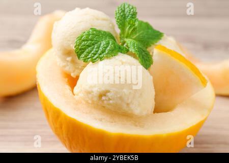 Scoops of tasty melon sorbet with mint in fresh fruit on wooden table, closeup Stock Photo