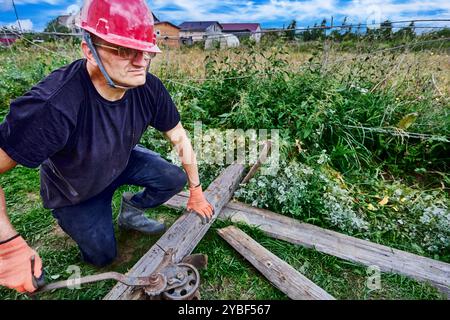 Construction worker uses manual cable winch to move load on suburban property. Stock Photo