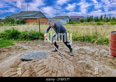 Construction worker compacts sand around septic tank lid using bayonet shovel. Stock Photo