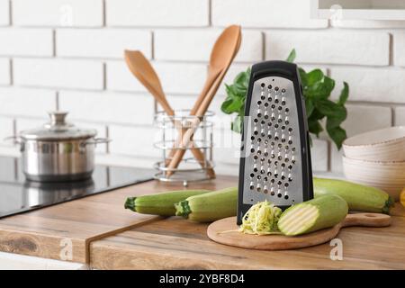 Grater with zucchini on table near white brick wall in kitchen Stock Photo