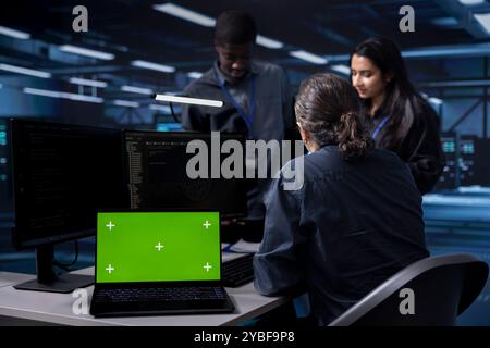 Multiethnic team using green screen screen laptop to check for signs of imminent failure in data center. Diverse staff members working on mockup notebook to prevent damages in server farm Stock Photo