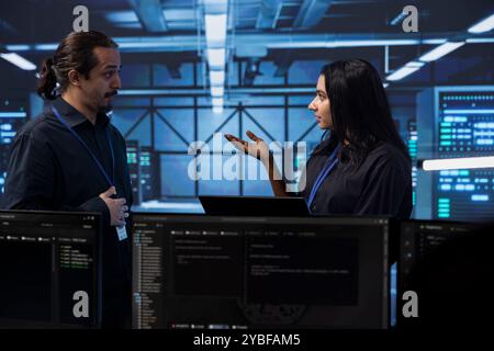 Programmers in server room discussing next steps after checking recovery plan and monitoring energy consumption. Colleagues in data center location talking about routine disk checks results Stock Photo