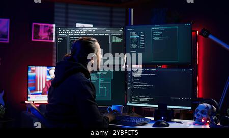 Hacker in secret hideout typing on keyboard, trying to hide online activity after stealing data. Scammer attacking victims computers using malware while trying to avoid being detected, camera B Stock Photo