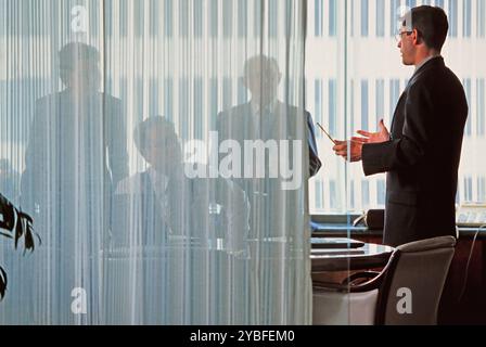 A presenter discusses important topics with colleagues in an office, with silhouettes of participants visible through a sheer curtain. Stock Photo