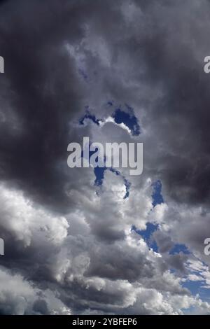 Gathering storm clouds loom overhead, filled with varying shades of gray and white, revealing patches of blue sky during the afternoon hours, suggesti Stock Photo