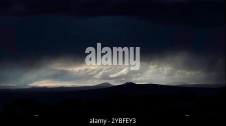 Clouds gather ominously over Sangre de Cristo mountains in New Mexico as twilight approaches, casting a moody atmosphere across the desert landscape Stock Photo