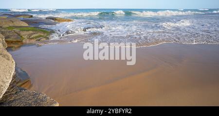 Surf waves breaking at sea and over rocks and rolling onto sandy beach east coast of Australia Stock Photo
