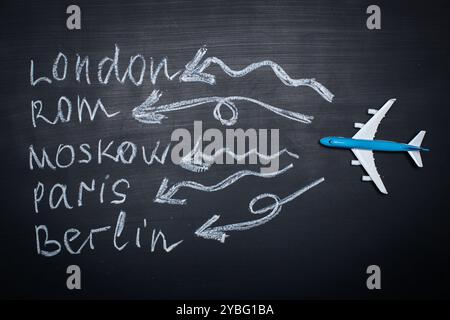 Traveling concept. Toy plane over chalkboard with cities written on it Stock Photo