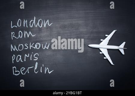 Traveling concept. Toy plane over chalkboard with cities written on it Stock Photo