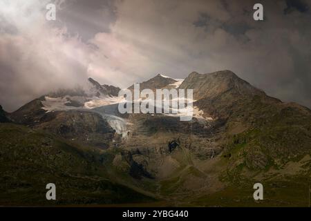 Dramatic View of Piz Bernina with Sun Rays Piercing Through Clouds at Bernina Hospiz, Switzerland Stock Photo