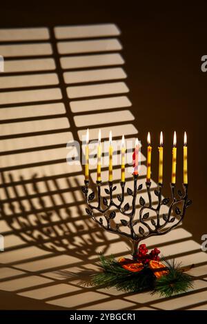 Menorah on a Window with Burning Candles and Pine Branch: the unity of Christmas and Hanukkah traditions during Christmukkah Stock Photo