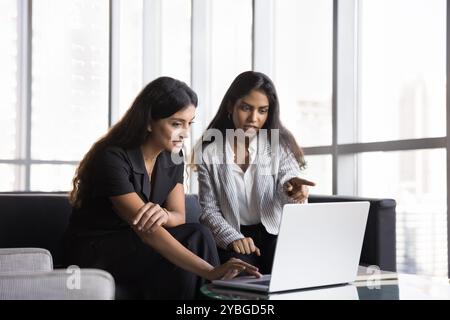 Two busy diverse female colleagues talking at laptop Stock Photo