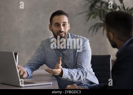 Positive handsome Latin businessman talking to business partner at workplace Stock Photo