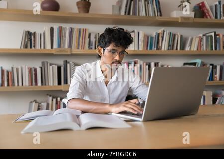 Serious young Indian student man in glasses typing on laptop Stock Photo