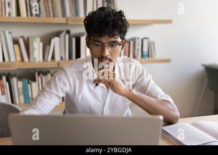 Focused handsome Indian student man studying online at laptop Stock Photo