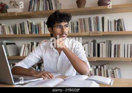 Thoughtful clever Indian student man in glasses writing scientific article Stock Photo