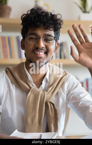 Cheerful positive young Indian student guy in glasses waving hello Stock Photo