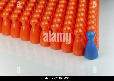 Conceptual orange game pawns and a blue play pawn as abstract display of inequality in color and number of Stock Photo