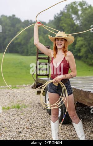 A beautiful redhead model poses in a country setting wearing cowgirl attire Stock Photo