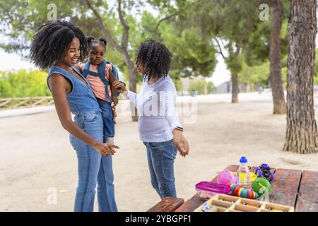 African multi- generation female family arriving at park to play next to picnic table with box with toys Stock Photo