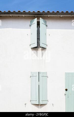 Windows with wooden light green painted closed shutters in white wall in old house in the Island of Re Stock Photo
